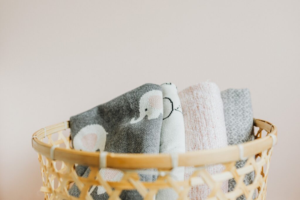 Soft patterned blankets arranged in a wicker basket against a neutral background.
